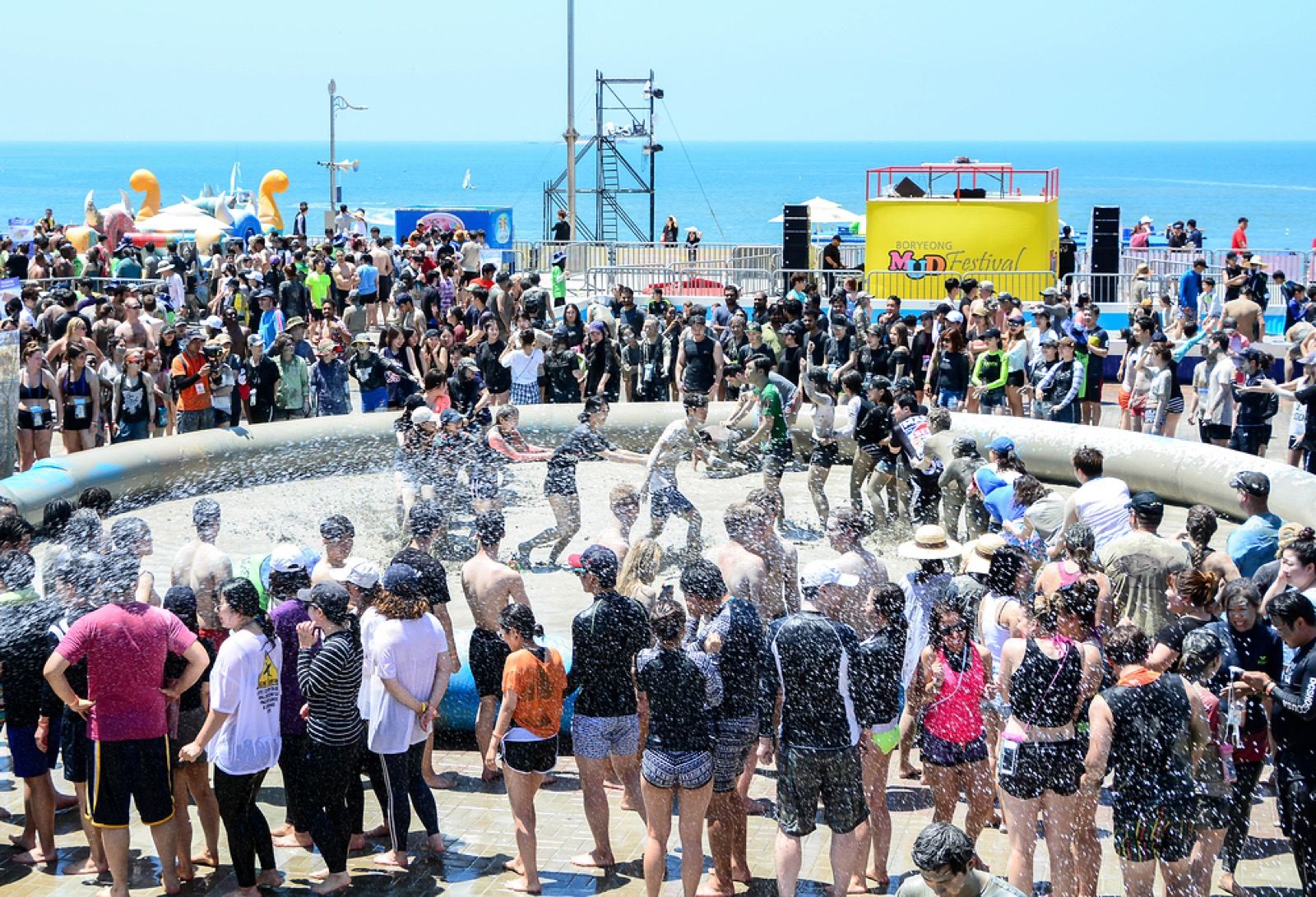 Crowds playing in a large mud pool by the sea at the Boryeong Mud Festival stage area on Daecheon Beach