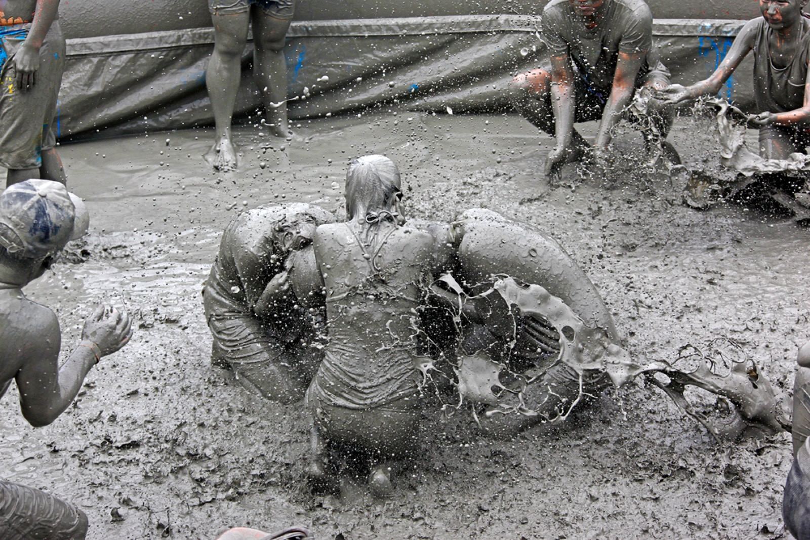 People wrestling and splashing in a gray mud pit at the Boryeong Mud Festival