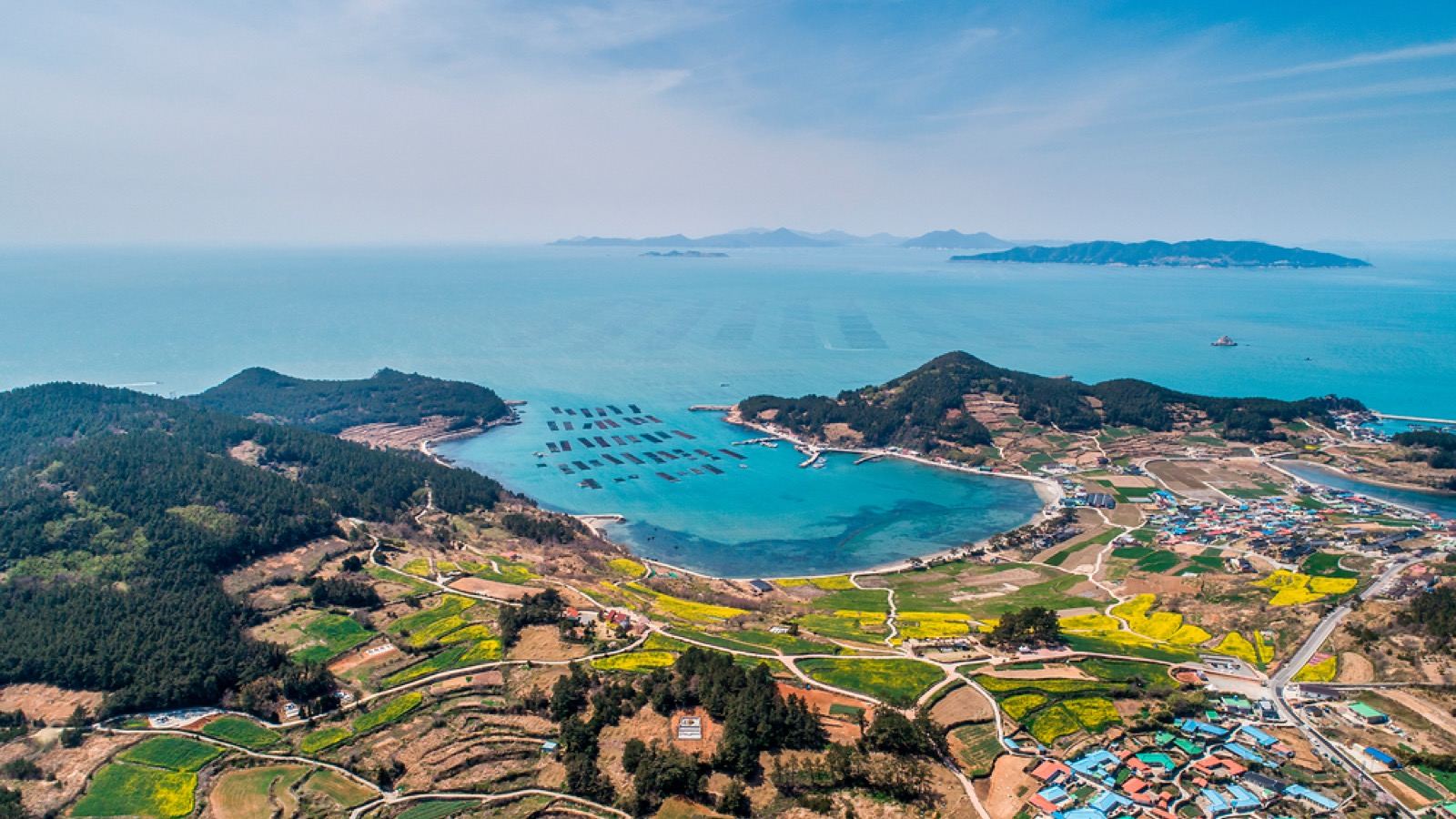 Aerial view of Cheongsando's green hills, a small harbor and terraced fields meeting a blue bay