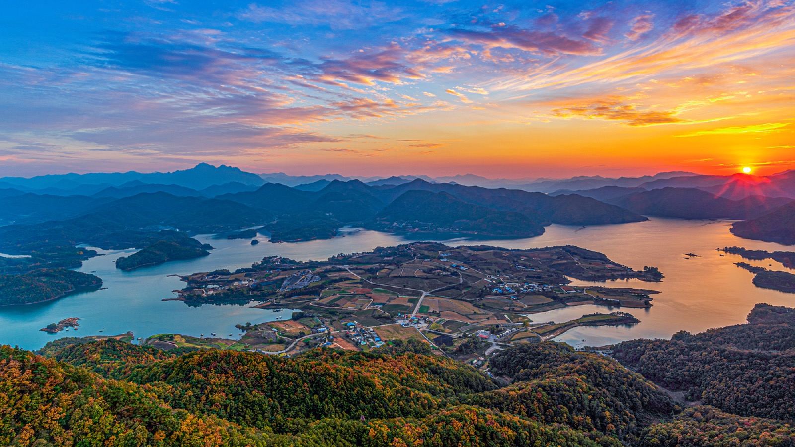 Chungju Lake at sunrise, islands and farmland reflected in calm water under an orange sky