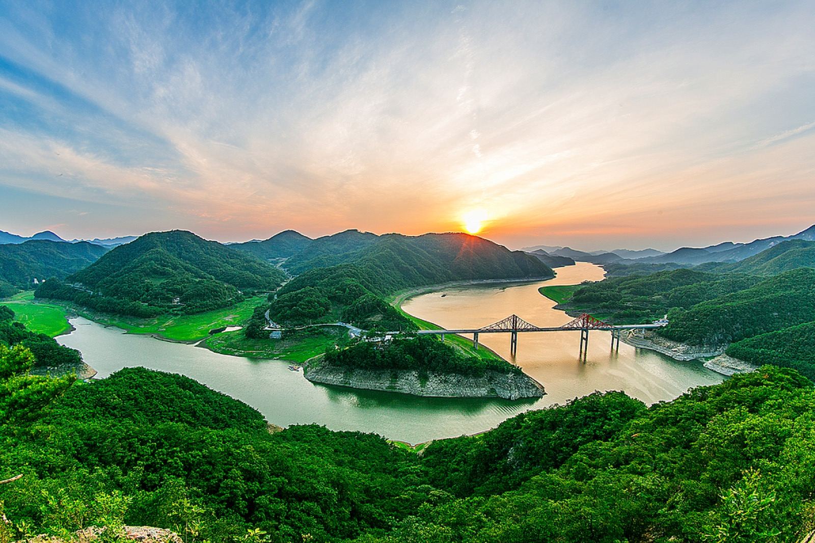 A steel bridge over Chungju Lake at sunset, forested hills glowing in the low light
