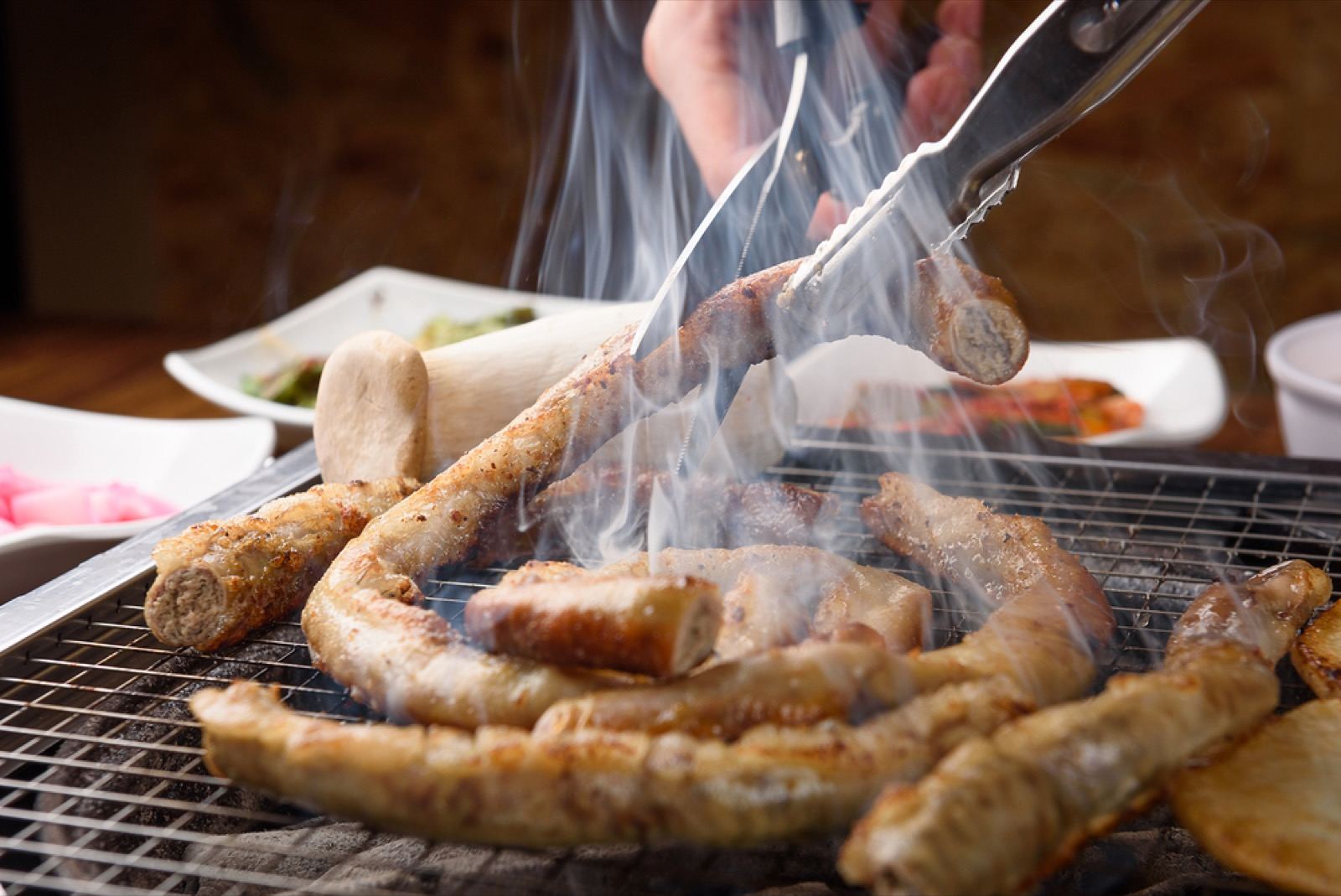 Coiled makchang grilling over a smoky tabletop grill in a Daegu restaurant, tongs turning the pieces