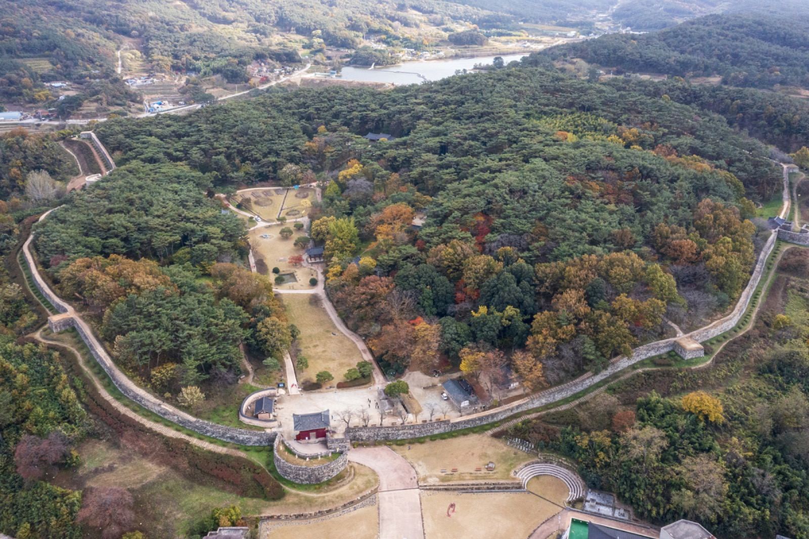 Aerial view of the oval stone wall of Gochang Eupseong fortress ringing a wooded hill in autumn