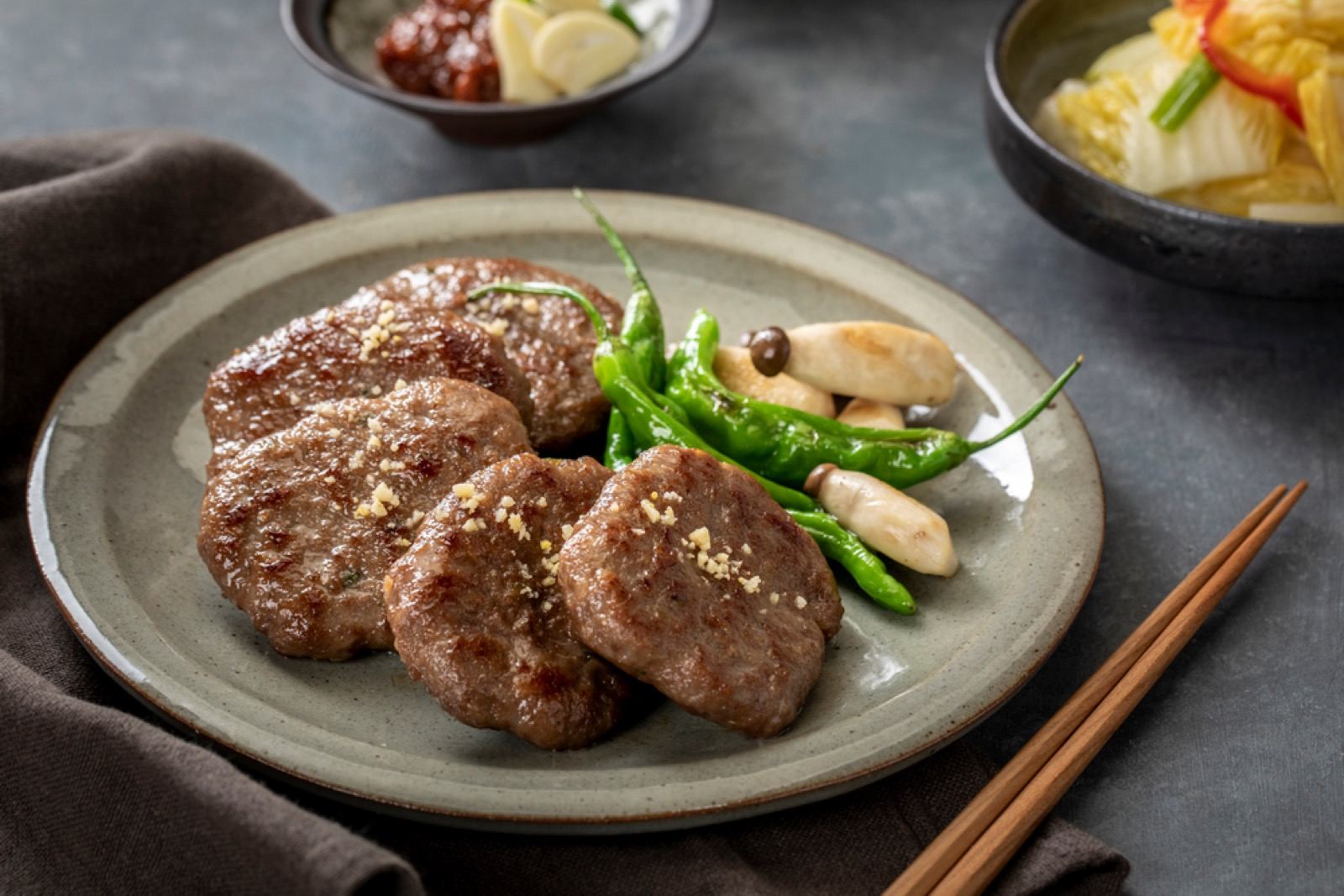A plate of grilled Gwangju-style tteokgalbi patties with green chili and garlic