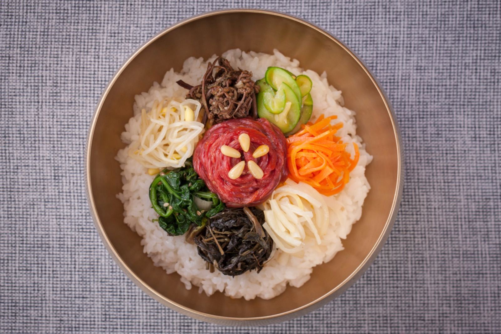 Jinju-style bibimbap in a brass bowl, raw beef and five colors of namul arranged over rice