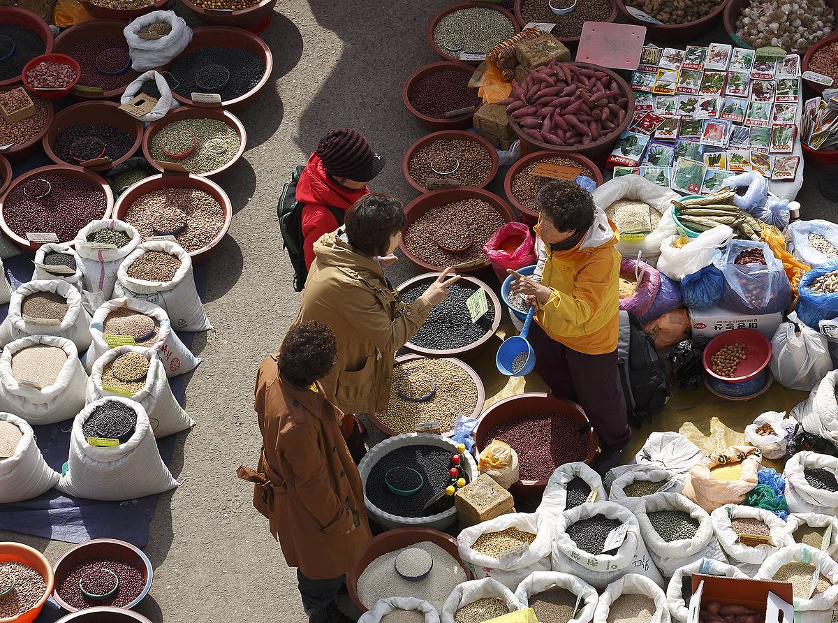 Shoppers browsing bowls of beans and grains at an open-air Korean market