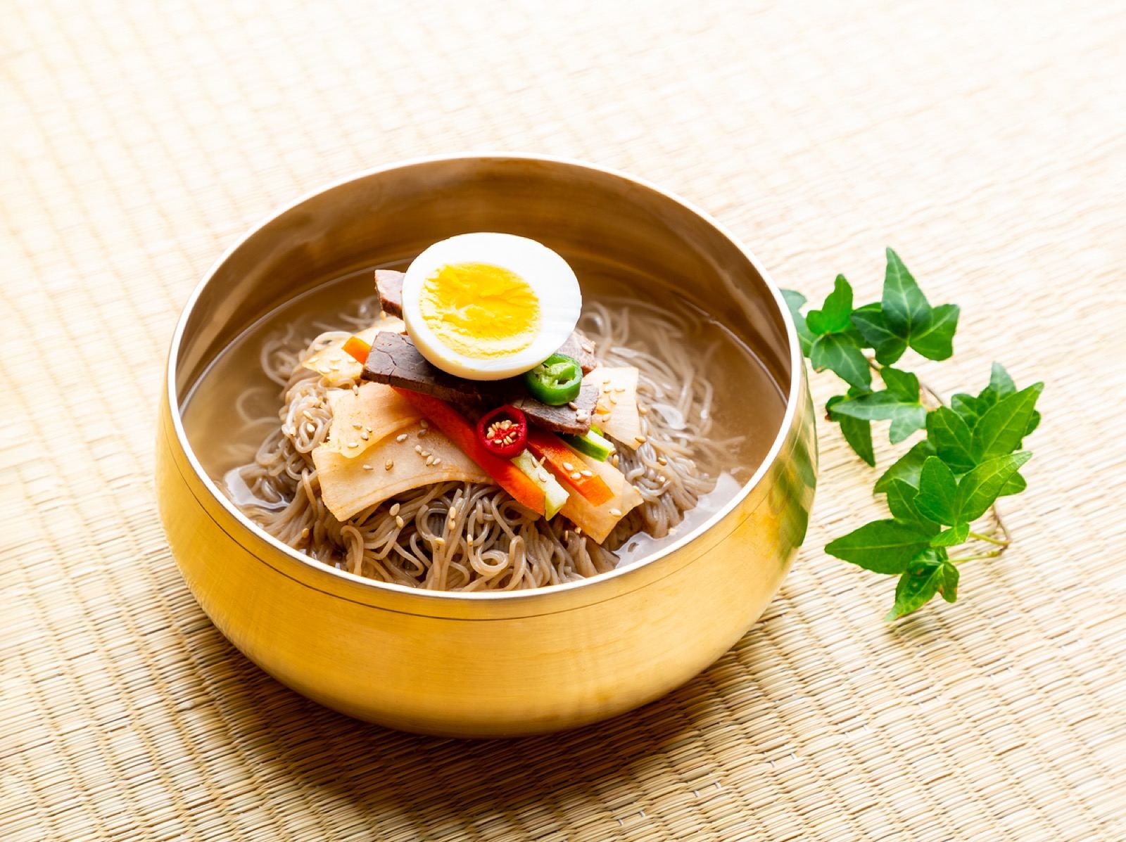 A brass bowl of mul-naengmyeon, buckwheat noodles in icy broth topped with egg, beef and cucumber