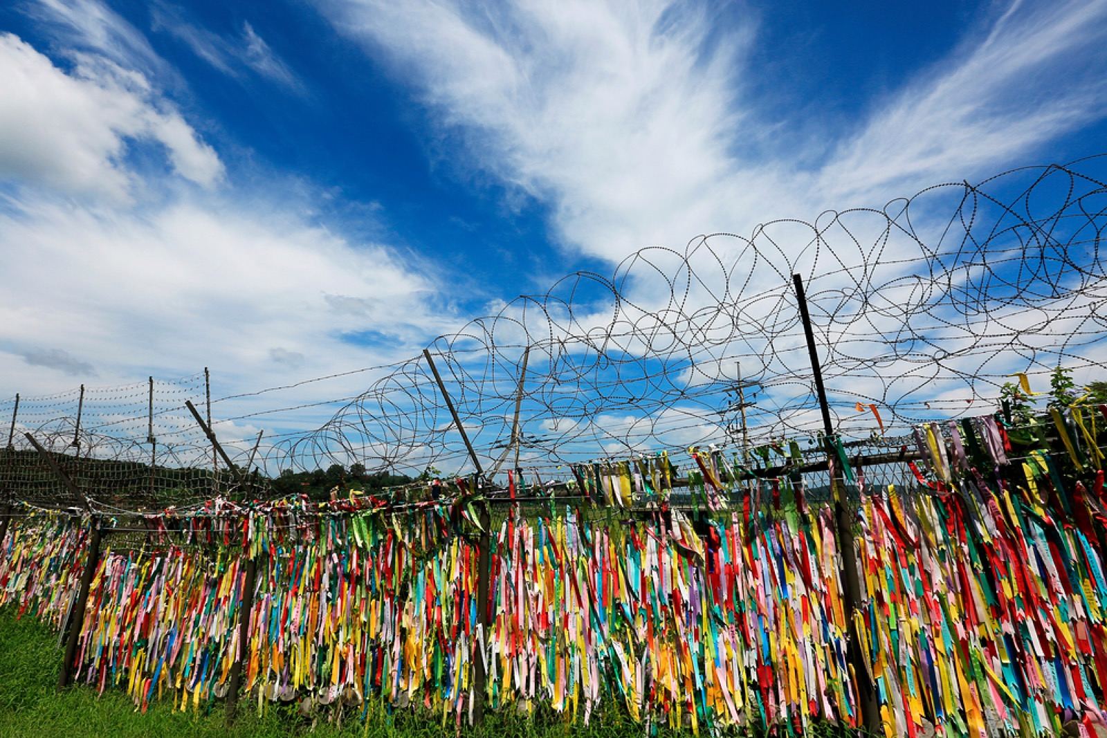 A barbed-wire fence near the DMZ hung with thousands of colorful prayer ribbons under a blue sky
