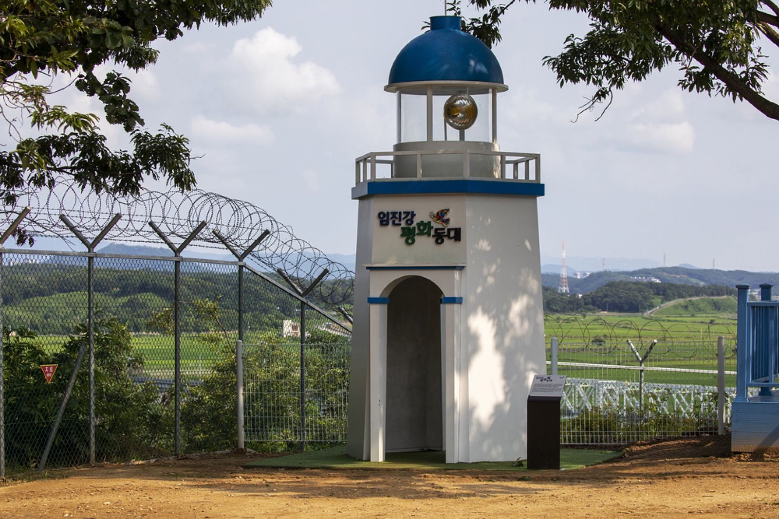 A small peace lighthouse beside the border fence at Imjingak, green fields beyond