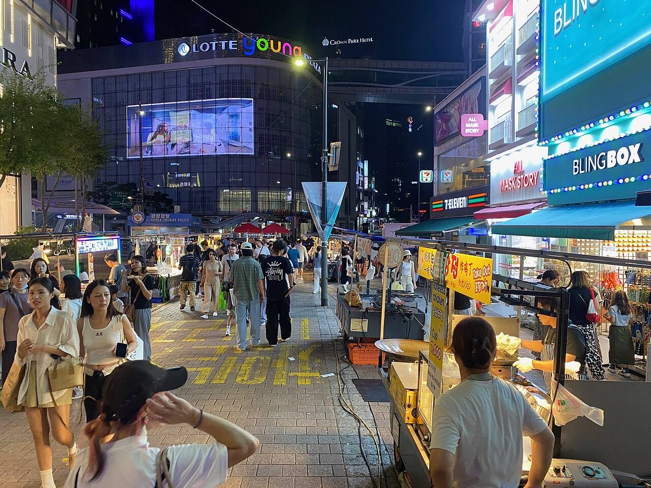 Street food stalls with price signs and shoppers at a Korean night market
