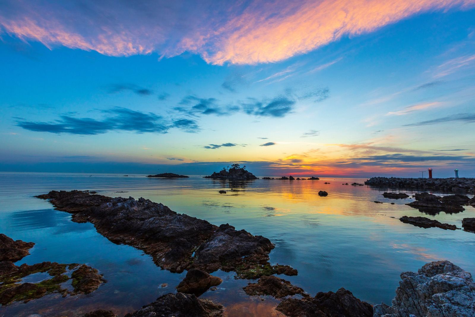 A rocky Samcheok shoreline with a sea stack silhouetted against a pink-and-orange dawn sky