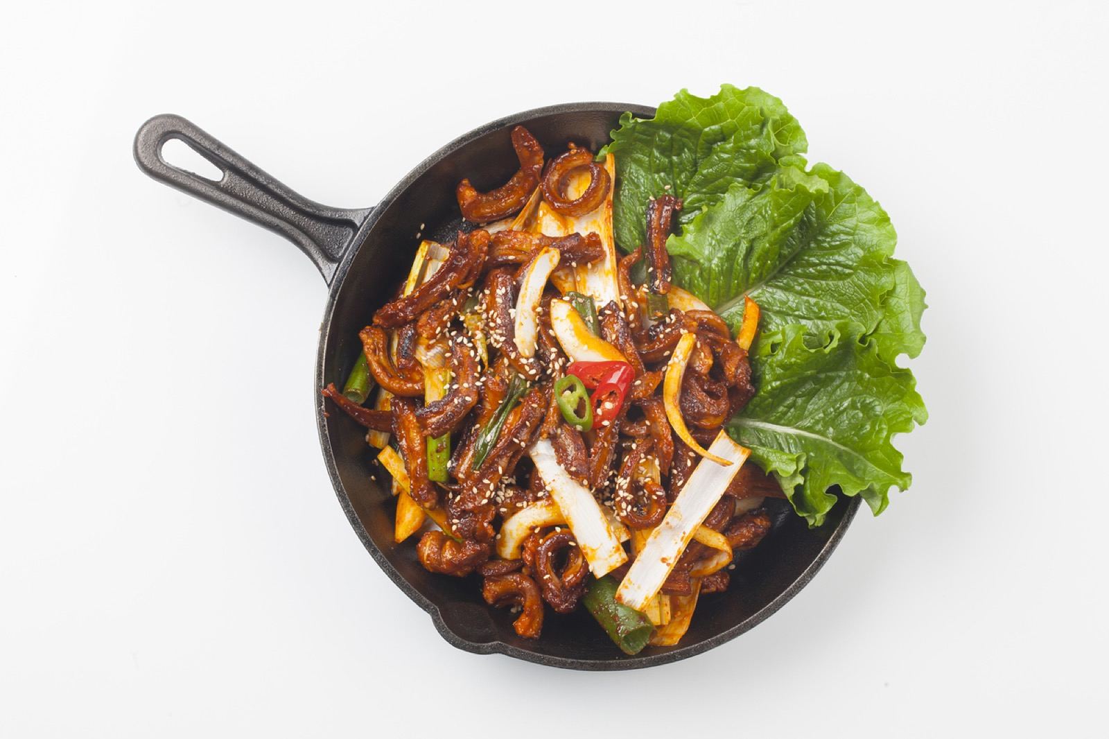 Seasoned gomjangeo stir-fried in a black pan with leeks, chili and lettuce on the side