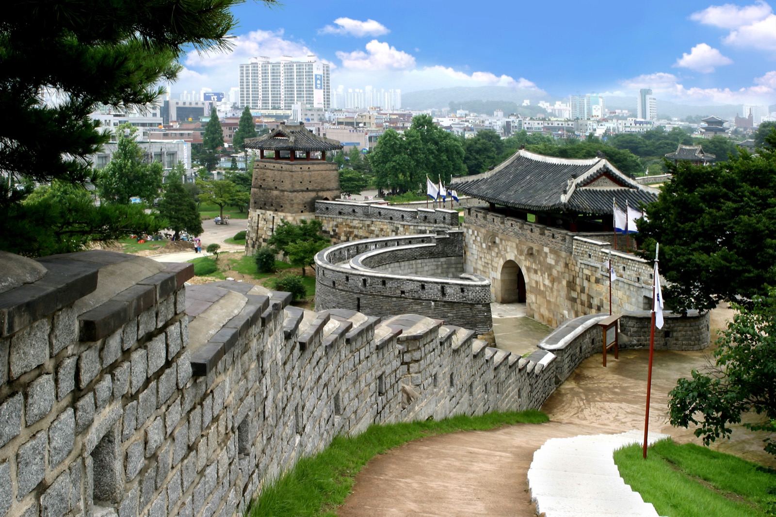 The stone rampart of Suwon Hwaseong Fortress curving toward a watchtower with the modern city behind