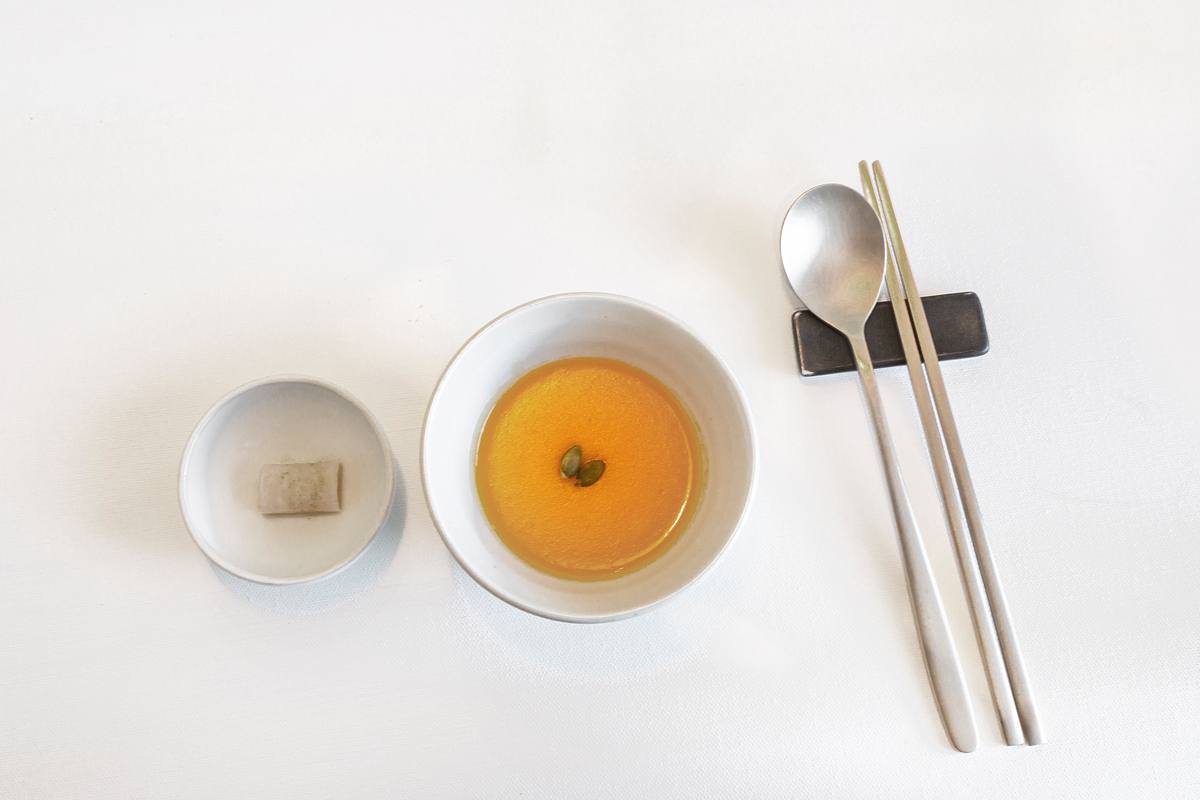 A minimalist Korean temple-food place setting with clear soup and a spoon