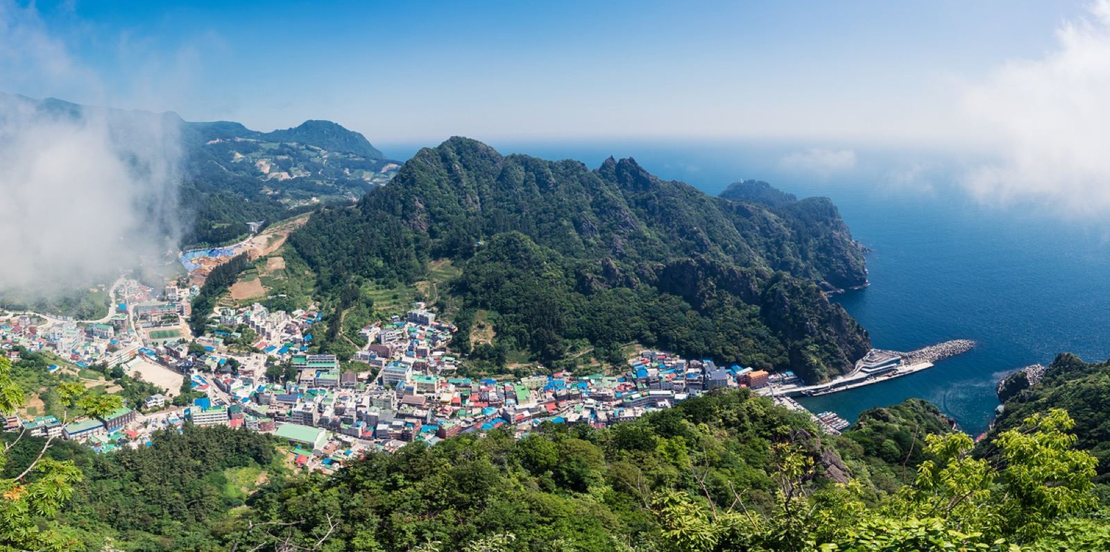 A colorful harbor village wrapped around steep green volcanic peaks on Ulleungdo island