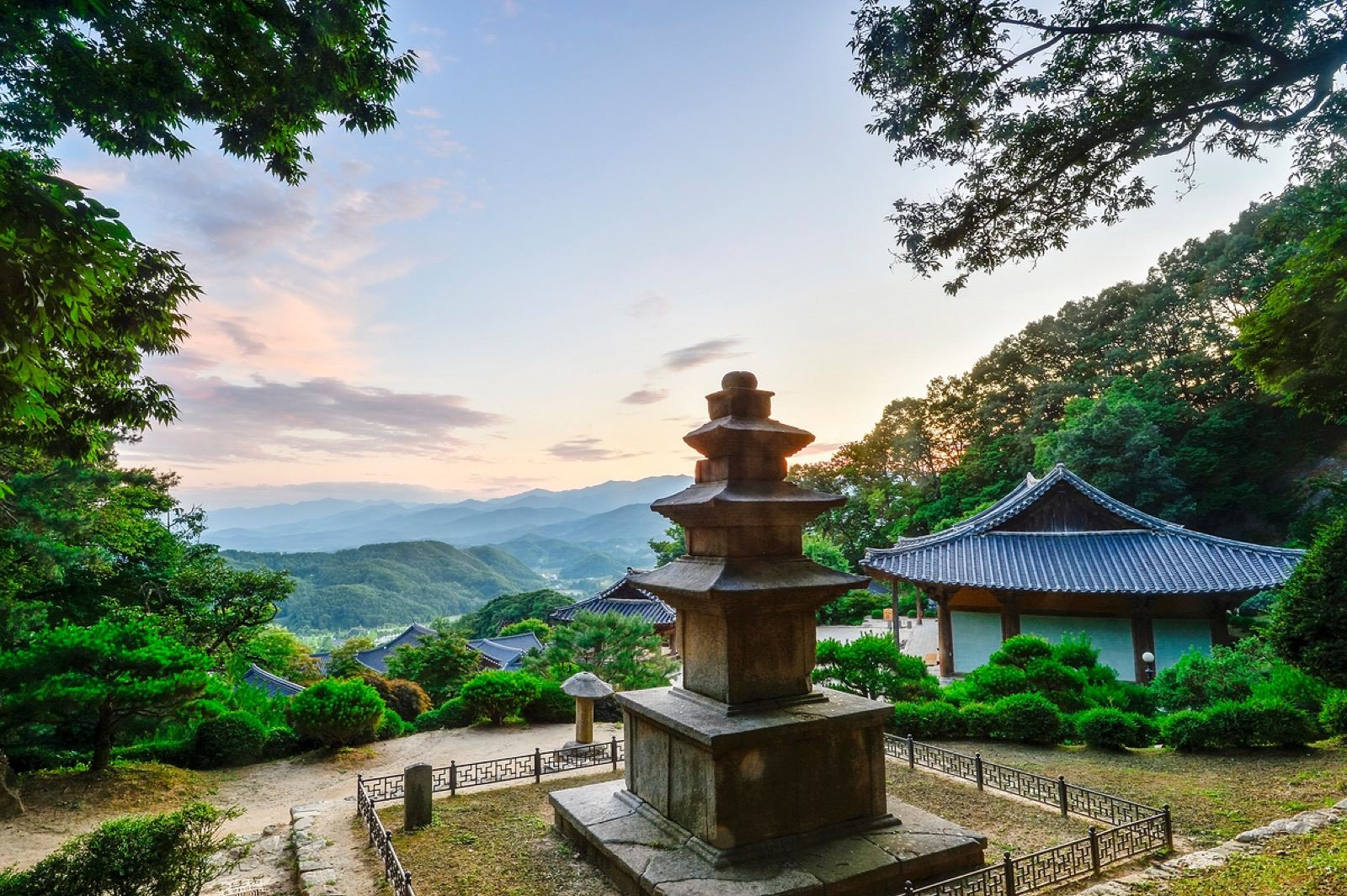 A stone pagoda in front of a wooden temple hall at Buseoksa, mountains glowing at sunset behind